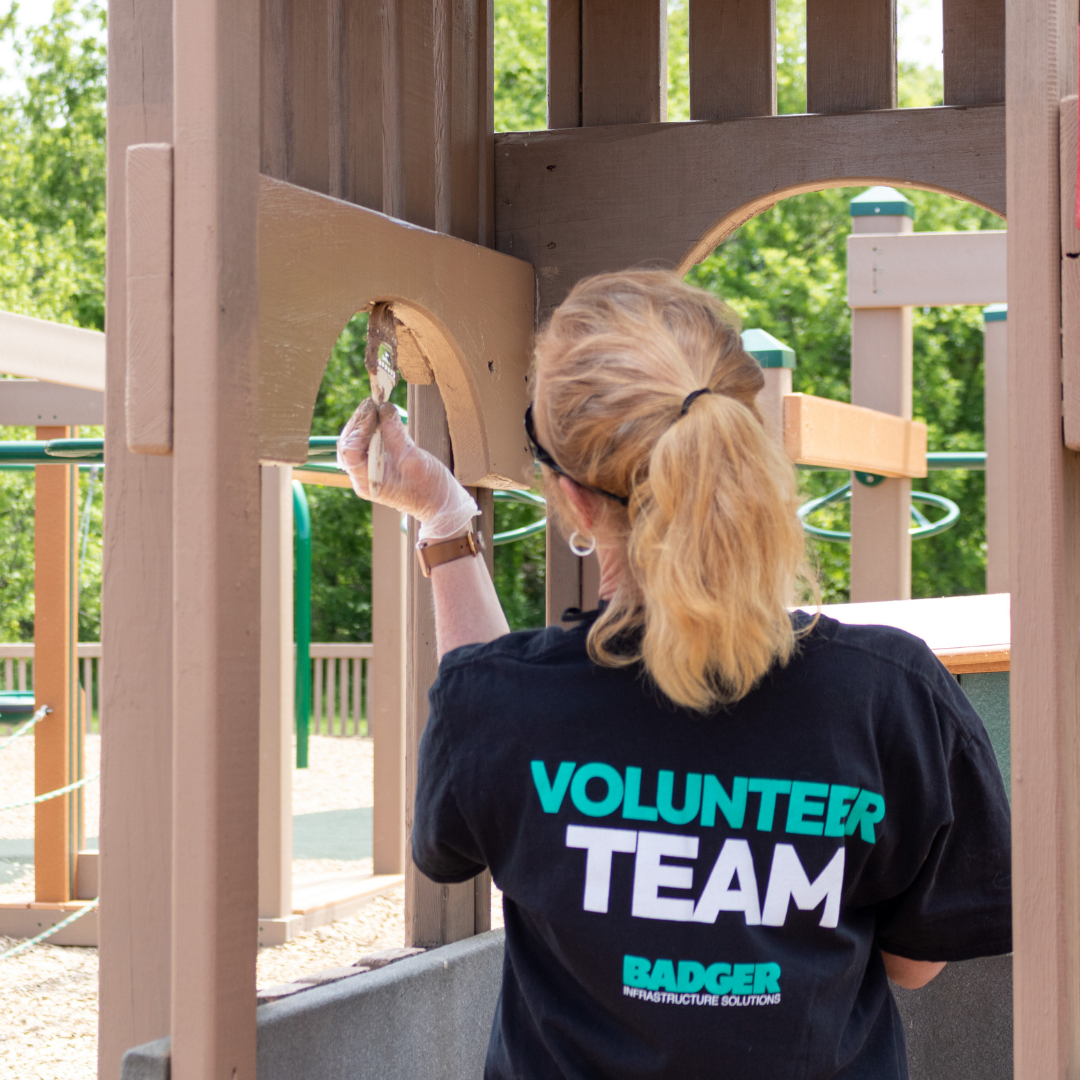 A woman paints to wooden playground structure at Blast Off Playground. 
